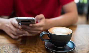 Person in red shirt holding phone in a coffee shop